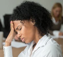 African american businesswoman feeling unwell from migraine pain touching forehead at team meeting