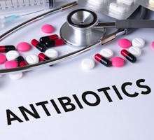The word antibiotics surrounded by pills and a stethescope