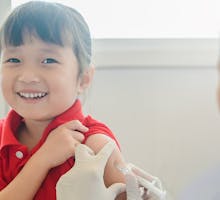 smiling child in red shirt gets COVID-19 vaccine for younger kids or is being vaccinated against flu