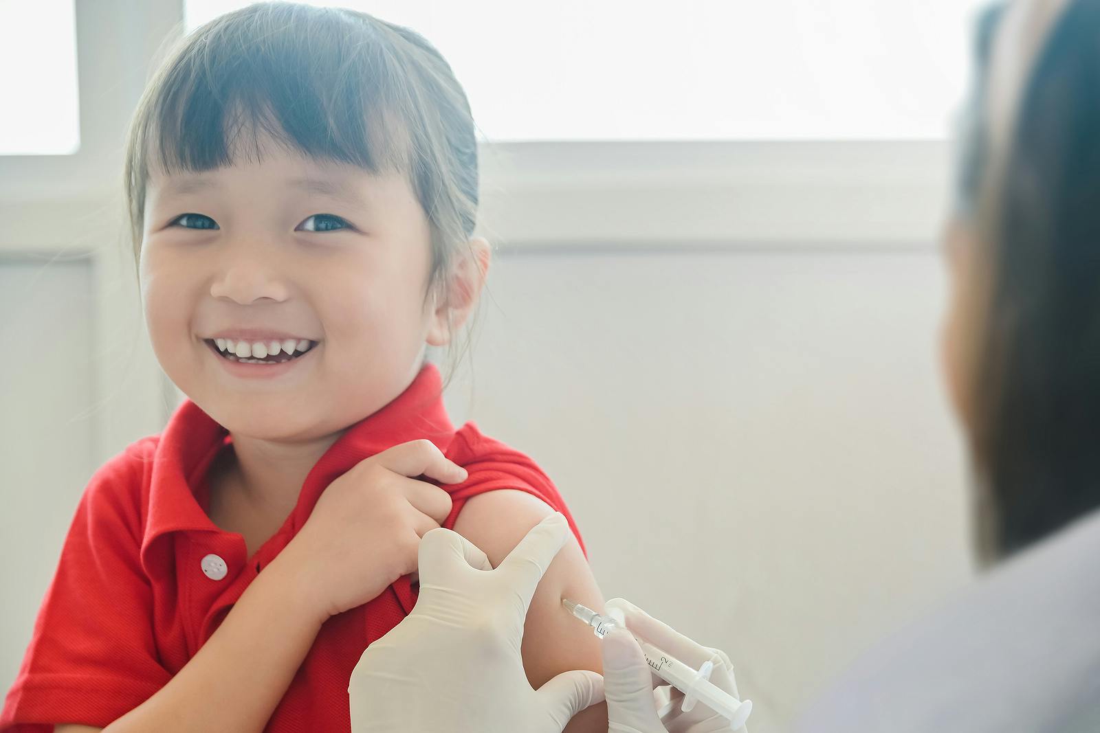 Asian Little child having Injection, Close-up Doctor injecting vaccination to arm of little girl her smile face and looking camera , vaccine injection for immunization health and medical concept
