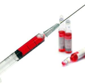 Vitamin B12 (cobalamin) in a syringe ready for injection with vials in the background; Vitamin B12 injections
