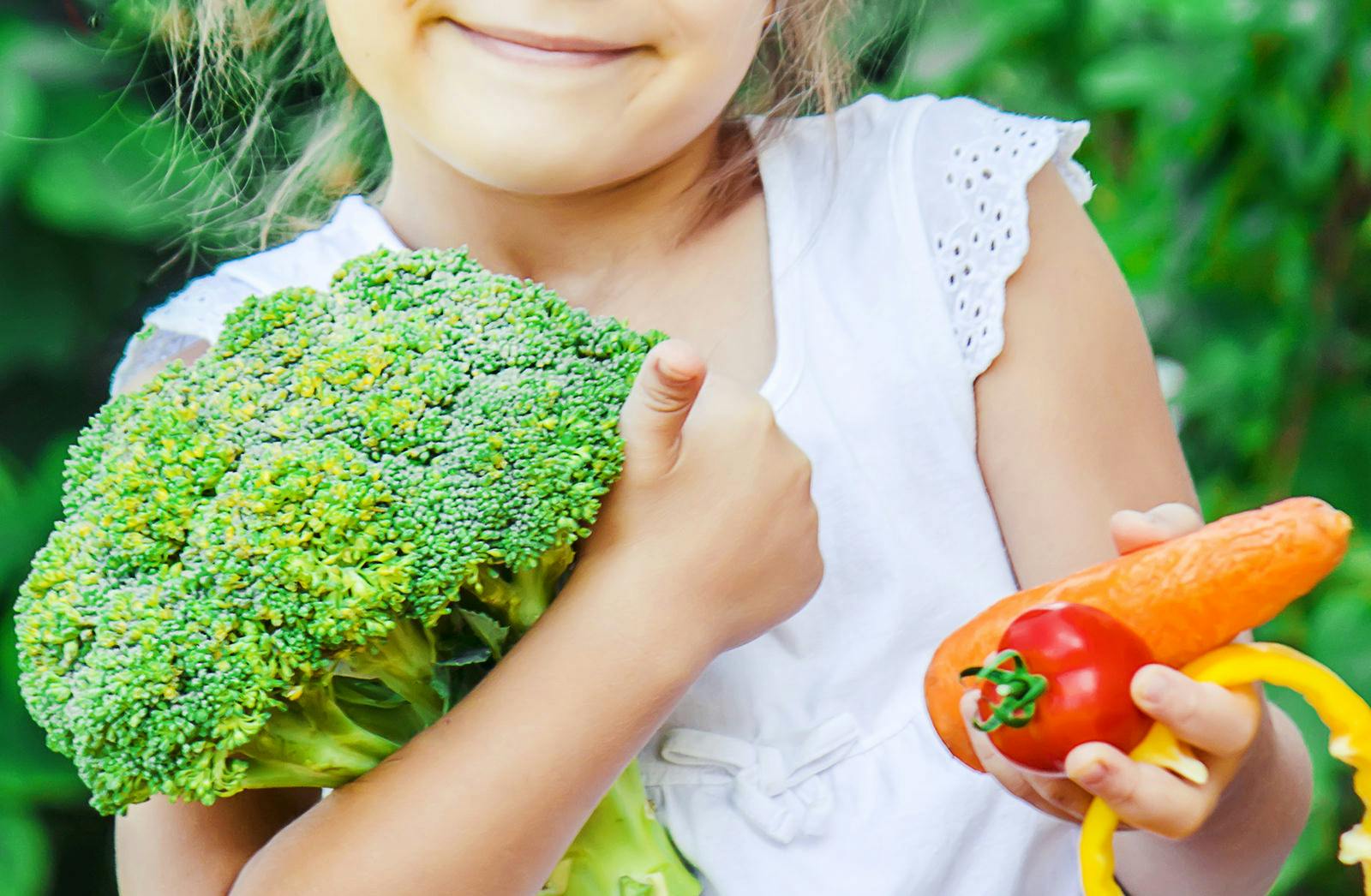 young girl holds colorful veggies