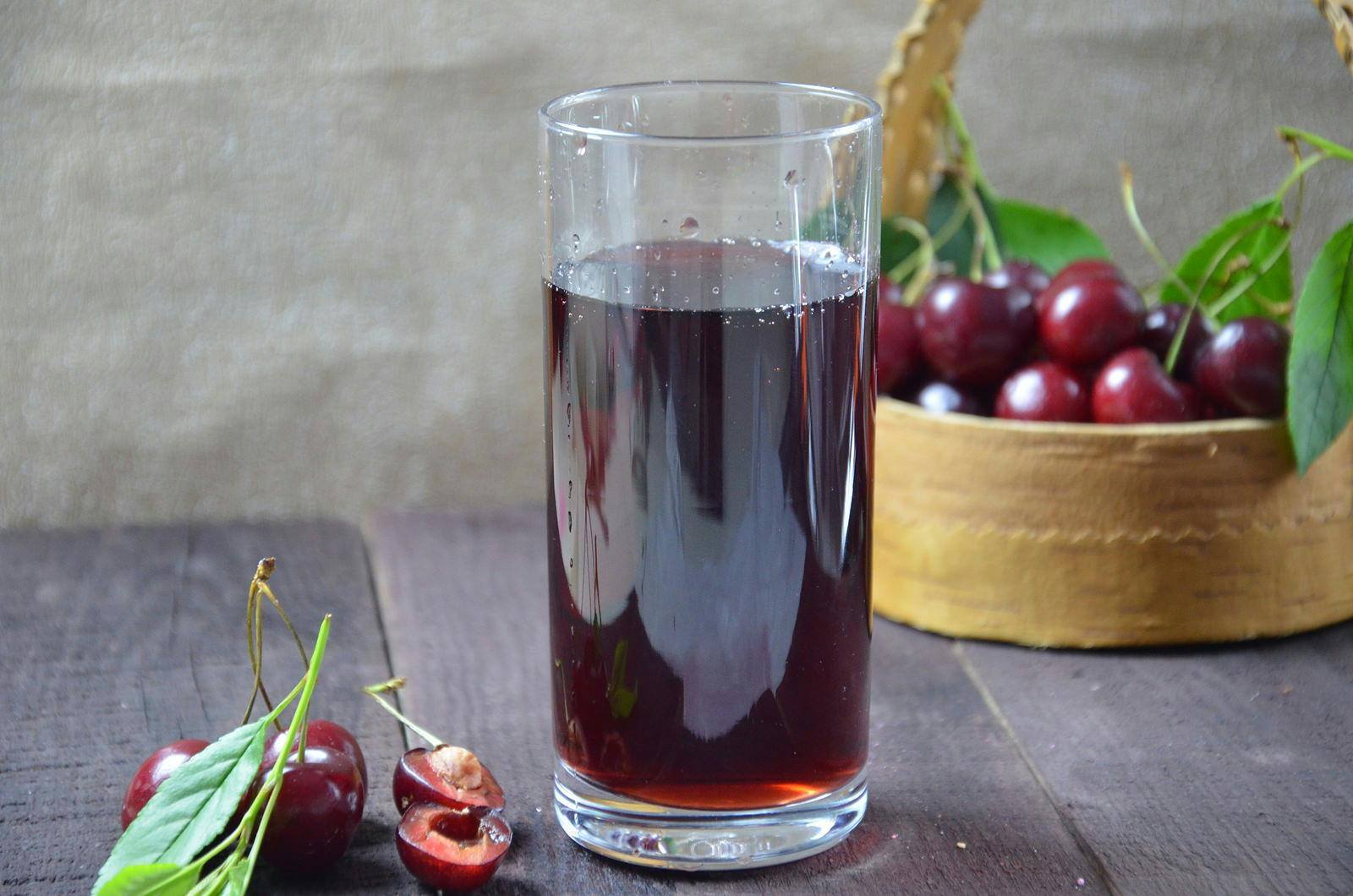 cold cherry juice in a glass and pitcher on wooden table with ripe berries in wicker basket