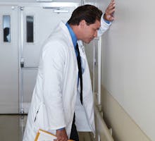 Depressed doctor leaning against wall in hospital corridor