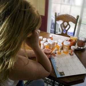 A woman struggling with all her medication, with many pill bottles on her kitchen table