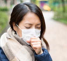 Woman wearing surgical facemask to protect from new virus and coughing into her hand