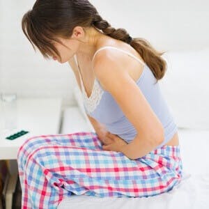 Girl with stomach ache sitting on bed suffers with irritable bowel syndrome