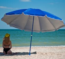 A young woman without sunscreen hides in the shade of a beach umbrella