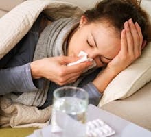 girl with cold or flu blowing her nose into a tissue