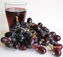 A glass of grape juice beside freshly washed grapes.