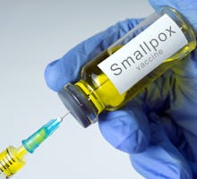 Syringe preparing smallpox shot, gloved hand holds vial