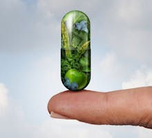 green capsule containing vegetables and fruits balanced on fingertip