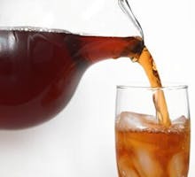 a pitcher of iced tea being poured into a glass of ice