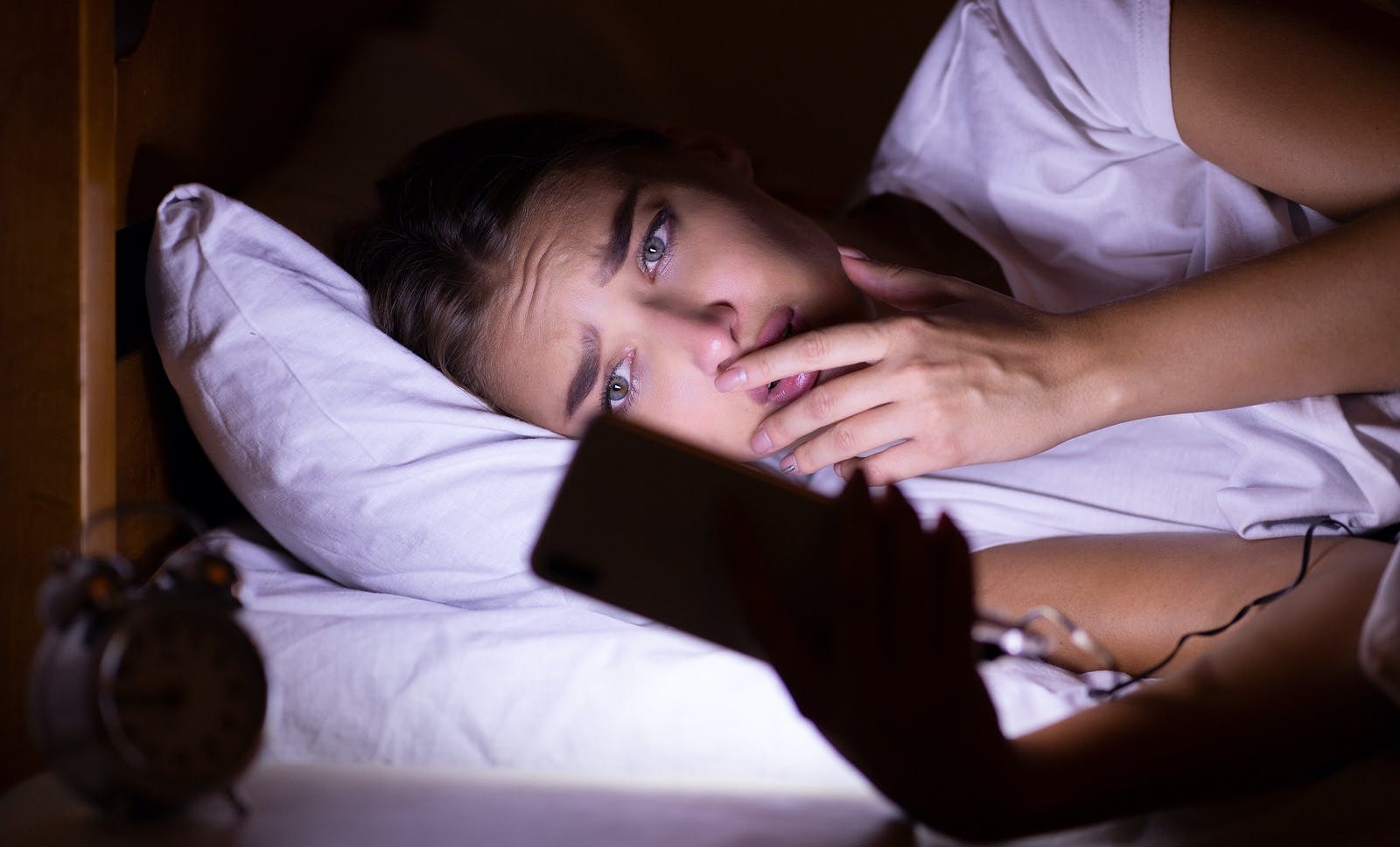 woman staring at cell phone in bed with anxious look on her face