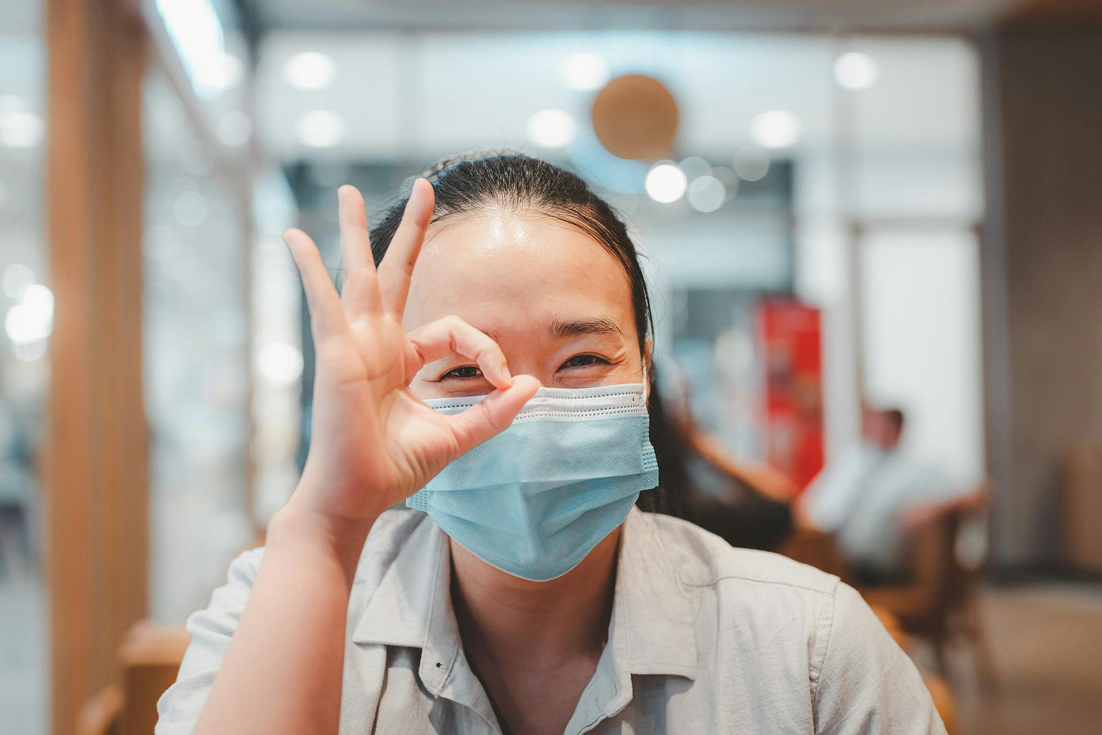 New normal of Asian lady wearing surgical face mask showing fine in sign language hand and smiling at camera Ways of life after the coronavirus COVID-19 outbreak , protect yourself in public places.
