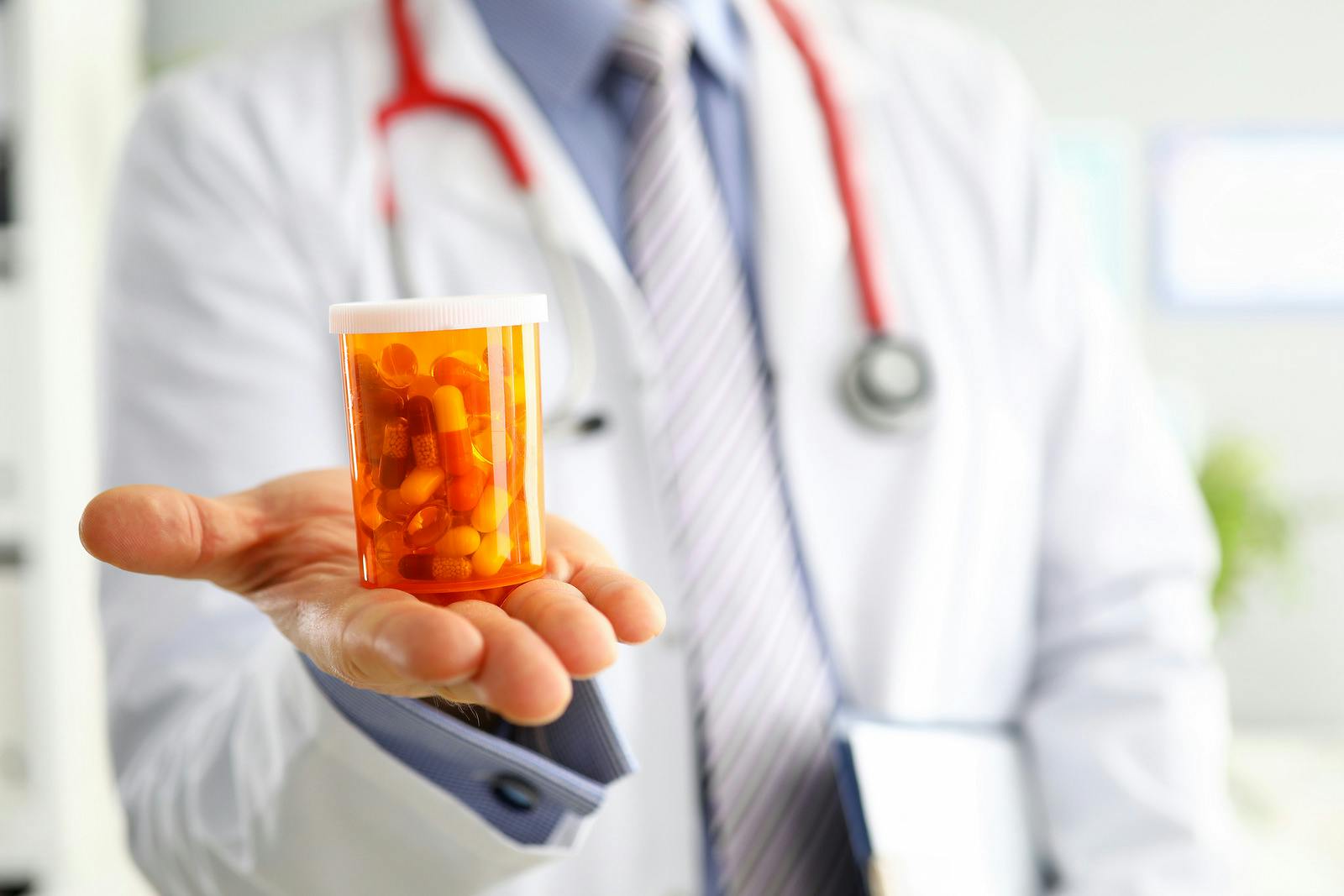 Hand holds out container of multiple pills doctors prescribe
