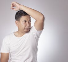 Man in T shirt sniffs his left armpit to see if he has horrible body odor