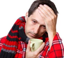 man with flu or cold wrapped in a warm blanket, holding a mug