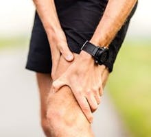 Runner holding sore leg knee pain from running or exercising jogging injury or cramp
