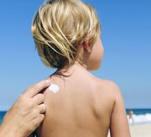 a mom applies sunscreen to the back of a little boy