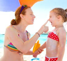 mother applying sunscreen to her daughter at the beach