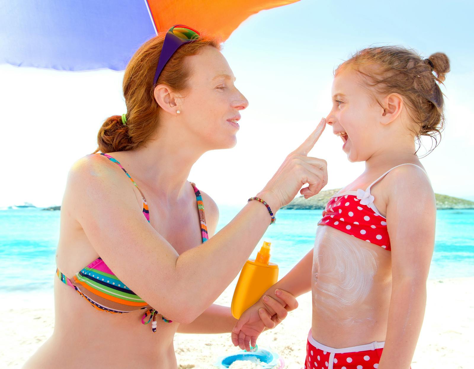 Daughter and mother in beach with sunscreen in bikini
