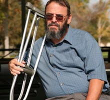 older gentleman resting on a park bench while holding his crutches