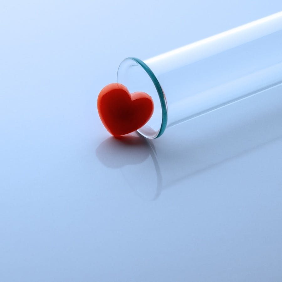 One red heart and a medical or laboratory glass test tube. Close-up. Copy space. Toned in blue.
