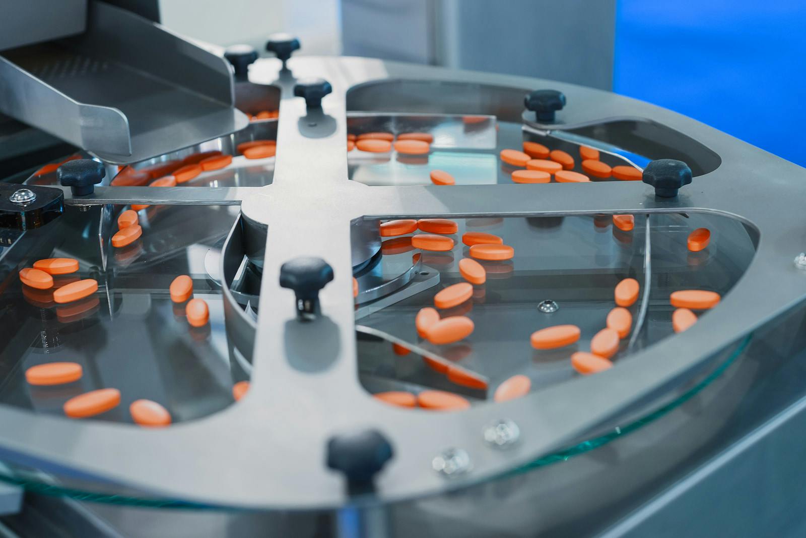 Pharmaceutical tablet manufacturing machine. Orange pills are sorted on a metal round conveyor.
