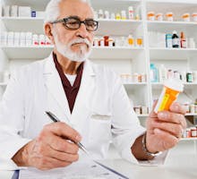 An older local pharmacist reads a pill bottle
