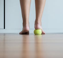 woman standing on tennis ball to relieve plantar fasciitis