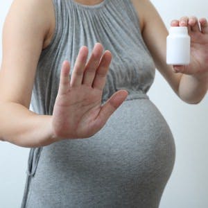 A pregnant woman holding a pill bottle in one hand making the halt gesture with her other hand