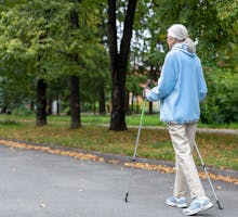 Older woman in blue jacket walks with poles to treat peripheral artery disease