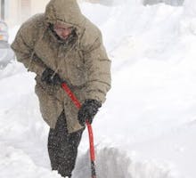 man in a parka shoveling a lot of snow