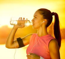 a female jogger with headphones in drinks from a water bottle
