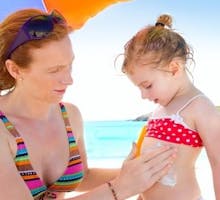 mother applying sunscreen to a young girl at the beach