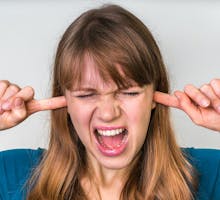 Woman closes ears with fingers because ears ring with tinnitus