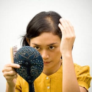 young woman checking her thinning hair in a mirror