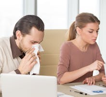 Sick man with handkerchief sneezing blowing nose while working with coworkers