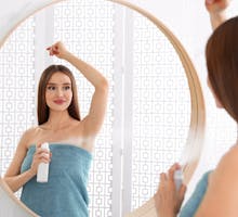 Young woman spraying on deodorant to underarms