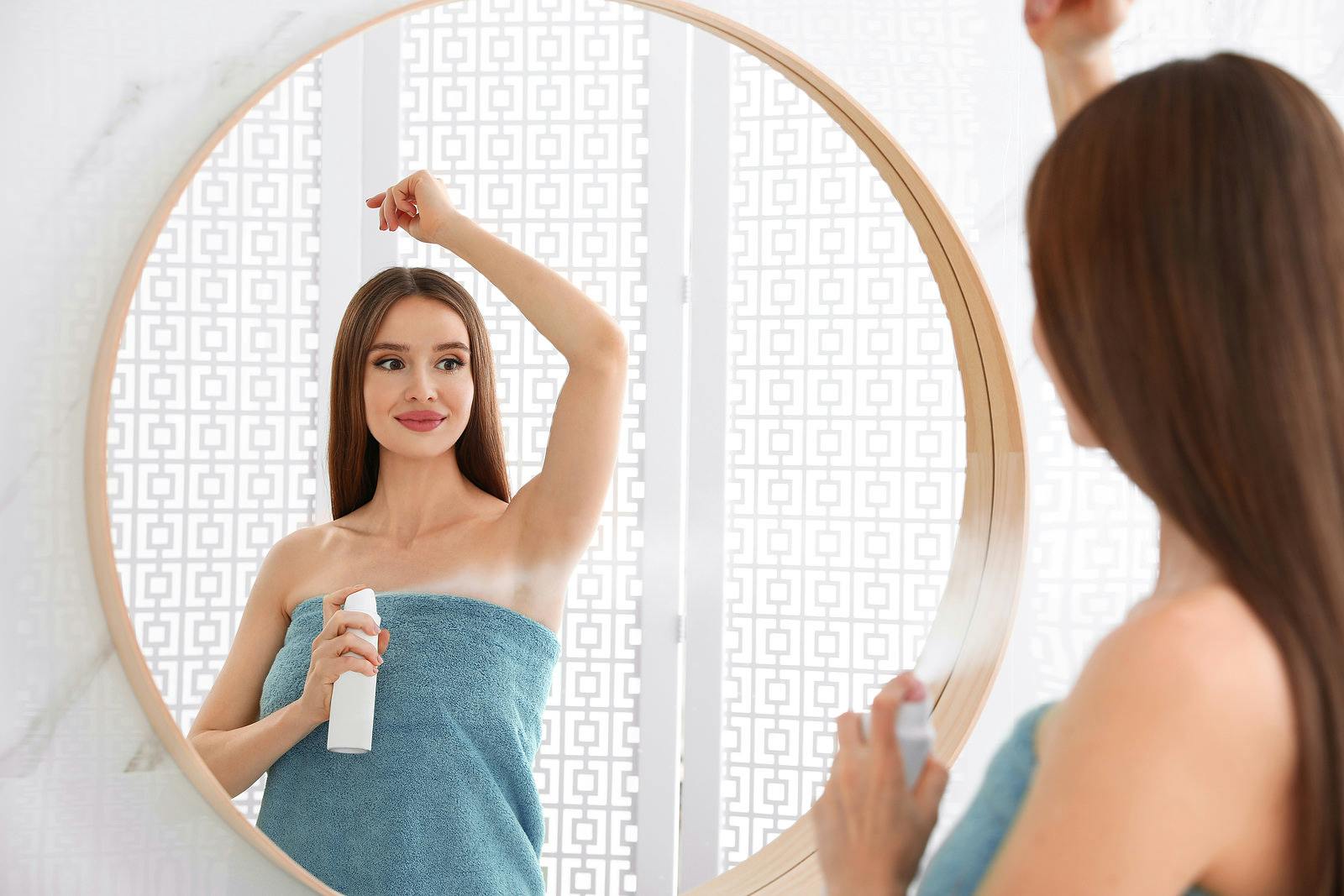 Young woman spraying on deodorant to underarms