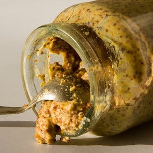 Spoon removing grainy dijon mustard from glass jar
