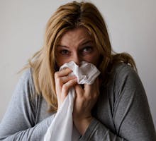 woman with the sniffles holds a tissue to her nose