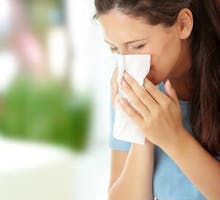 a woman with allergies or a cold blows her nose into a tissue